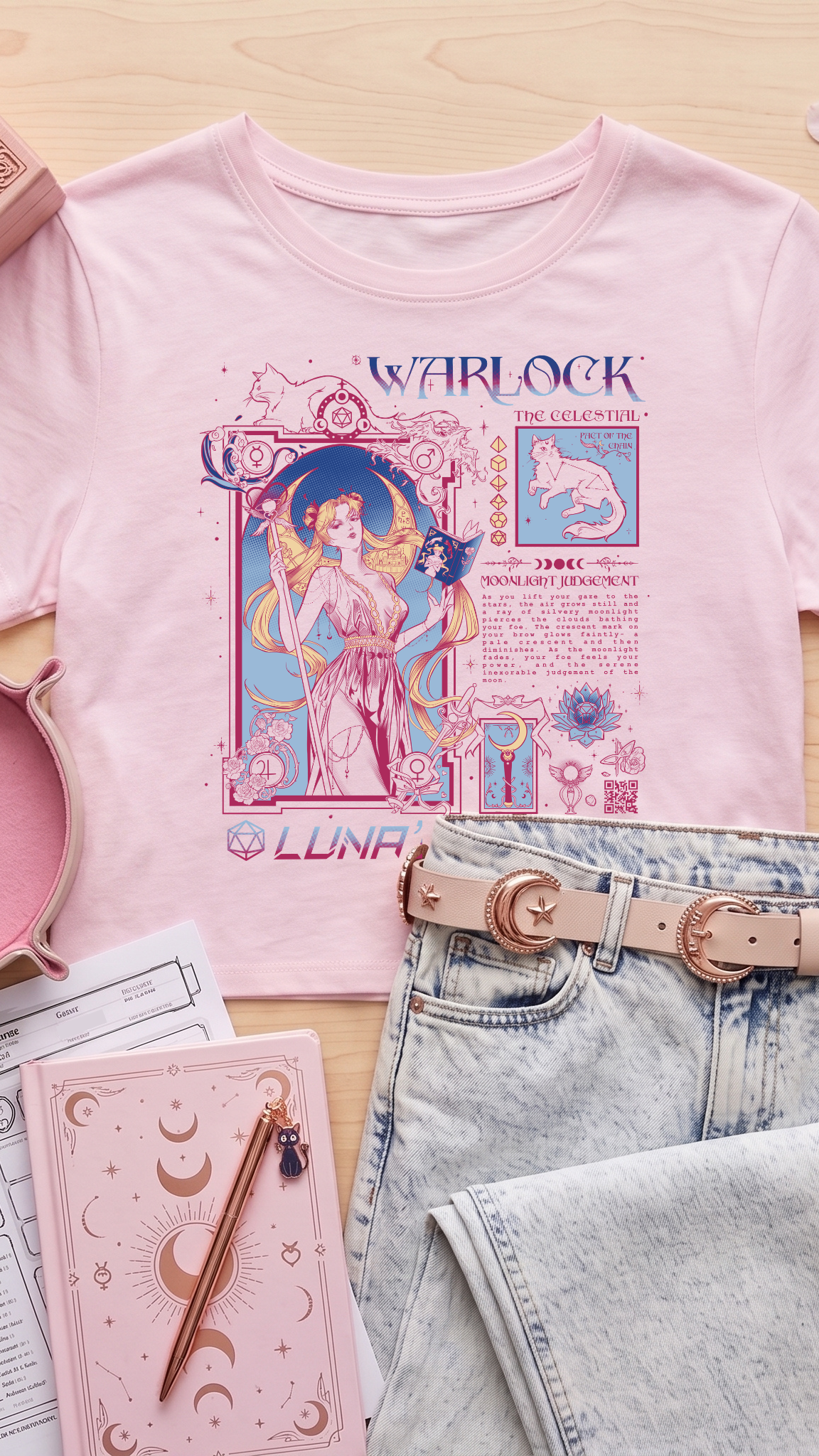 A styled flat-lay of a light pink graphic T-shirt featuring a celestial Warlock design, paired with light-wash jeans, a pink moon belt, and pink accessories on a light wood background.