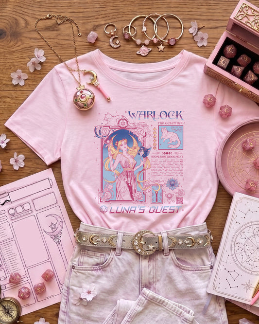 A styled flat-lay of a light pink graphic T-shirt with celestial artwork and the text 'WARLOCK' and 'LUNA'S GUEST', paired with pale pink jeans and a decorative belt, surrounded by pink accessories on a wooden surface. The shirt design is a Warlock inspired by Sailormoon and 90s magical girls. Anime mixed with Dungeons and Dragons