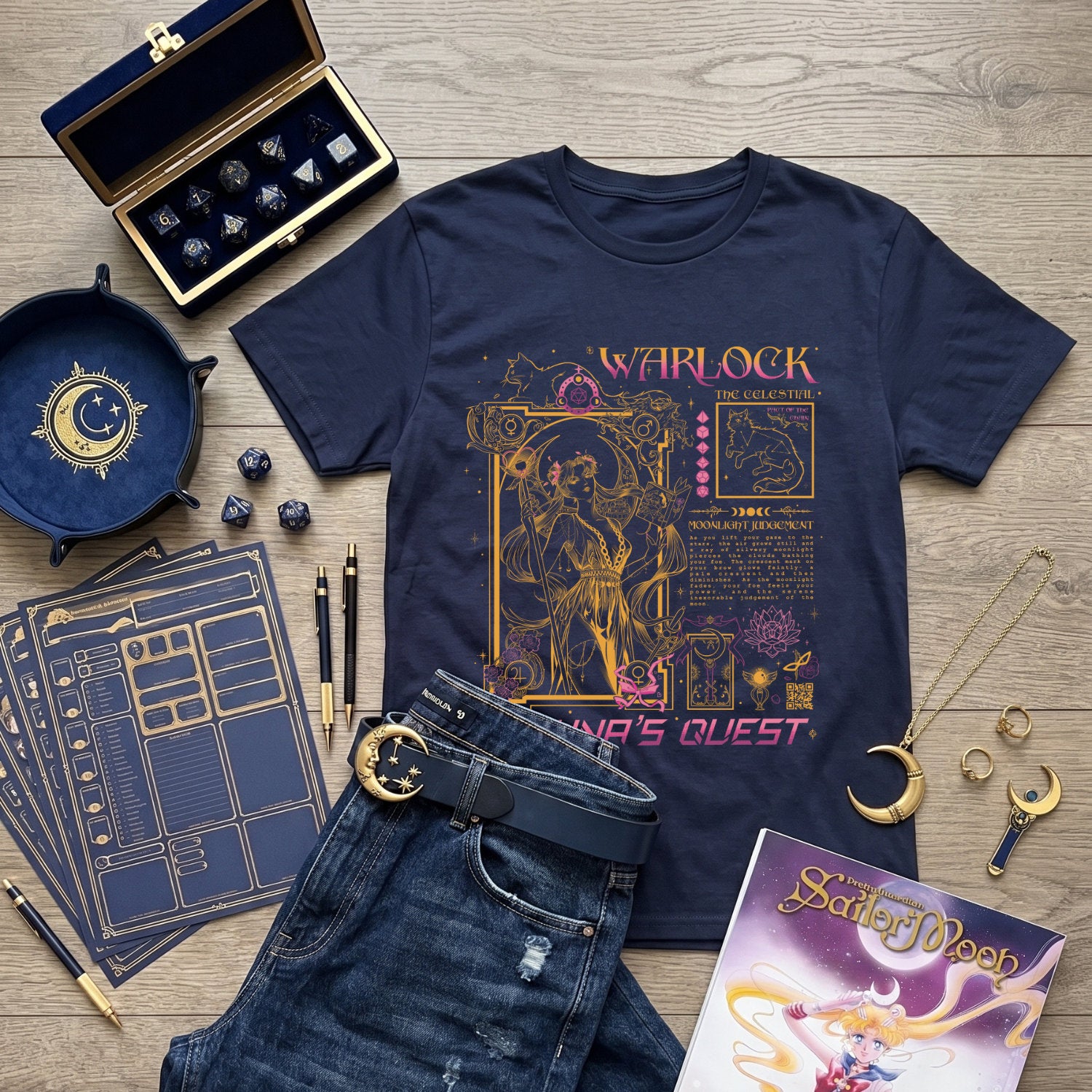 A navy blue graphic T-shirt laid flat on a wood surface, styled with a dark blue journal, black pen, gold compass, moon pendant, dice, jewelry, and a Sailor Moon book. The shirt features a fantasy Warlock inspired by Sailormoon and 90s anime magical girls.